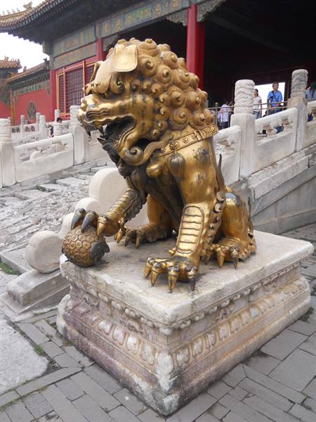 Gilded bronze lion at the Forbidden City, beside marble balustrades and visitors