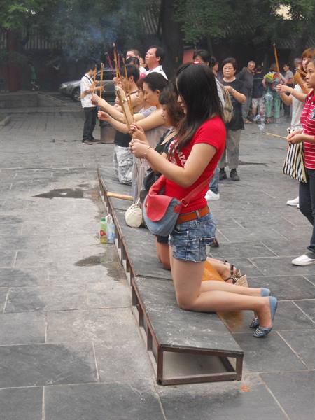 Women kneel praying with incense sticks in a temple stone courtyard