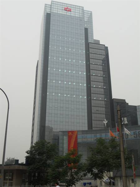 Glass skyscraper with red logo, hazy sky, trees and flags at base