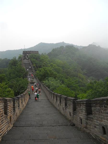 Tourists walk on the Great Wall among green misty mountains