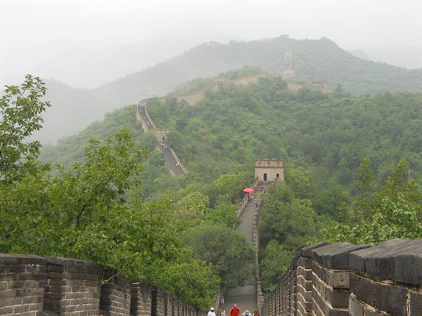 Tourists climb the Great Wall of China past stone towers in mist