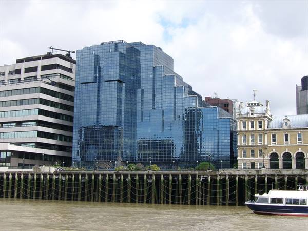 Blue glass office tower by the Thames, boat moored in front of wooden pilings