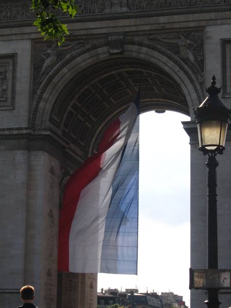 French flag waving beneath the Arc de Triomphe with a street lamp nearby