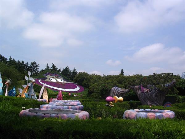 Alice in Wonderland sculptures among green hedges, Cheshire Cat's giant grin