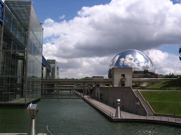 The mirrored sphere at Parc de la Villette reflects clouds beside the glass greenhouses