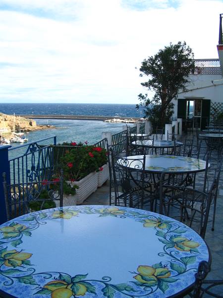 Terrace over Ponza harbor with lemon-painted ceramic tables, wrought iron chairs and geraniums