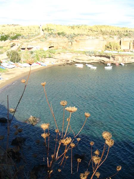 Small beach with moored boats, rocky cliffs and dry plants in the foreground