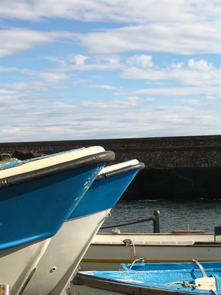 Blue boats moored near a black volcanic stone pier