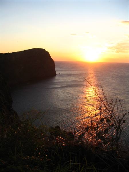 Low sun reflects on the sea beside a dark cliff
