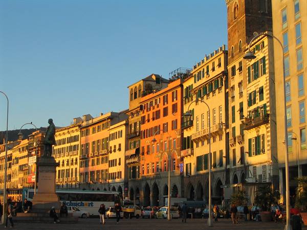 Bronze statue on pedestal in Genoa square, colorful buildings in evening light