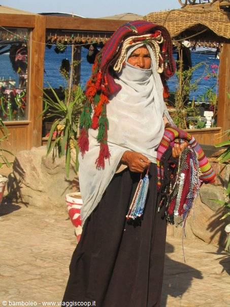 Veiled Bedouin woman sells colorful bracelets by wooden stalls overlooking the sea