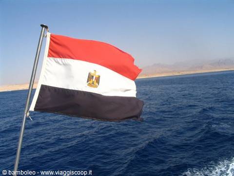 Egyptian flag waving on a boat sailing past desert coastline