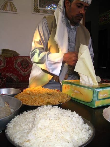 Man in white turban serving rice and traditional dishes on a table