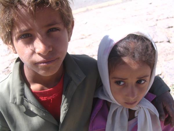 Boy and girl in light headscarf pose on sunlit paved street