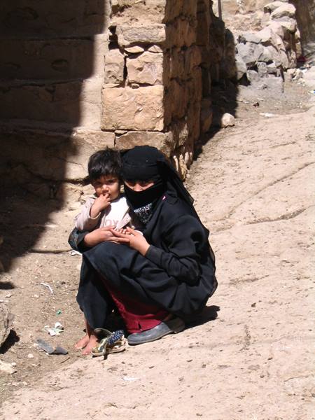 Veiled woman in black crouching with child beside stone walls