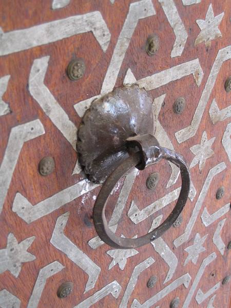 Metal ring knocker on wooden door with white geometric inlays and studs