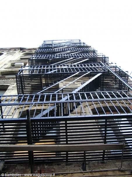 Black iron fire escape zigzagging up a brick facade, low angle