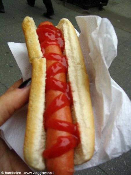 Hot dog with ketchup wrapped in a paper napkin, held on the street