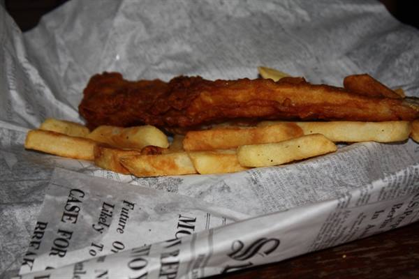 Battered fried fish with chips on newspaper, warm natural light