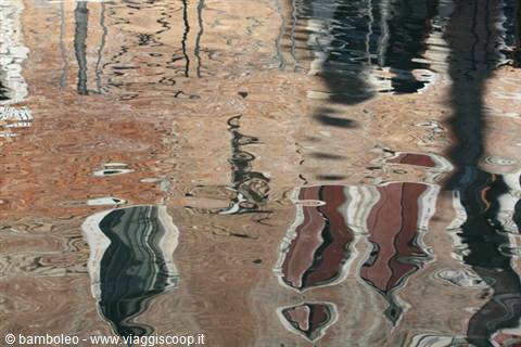 Reflections of colorful buildings and mooring poles in a Venice canal