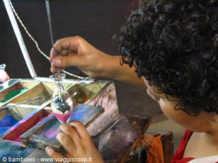 Artisan pouring colored sand into a small glass bottle, craft workshop
