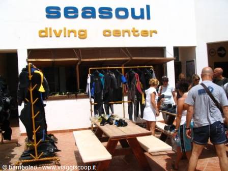 Wetsuits hanging outside Seasoul Diving Center, people gathered around wooden tables