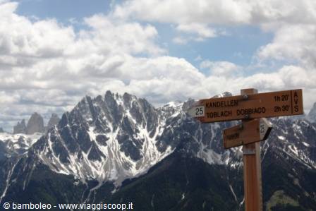 Wooden trail signpost toward Toblach and Dobbiaco among snowy Dolomite peaks