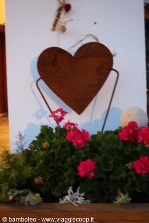 Rusty iron heart among pink geraniums, decoration on white wall