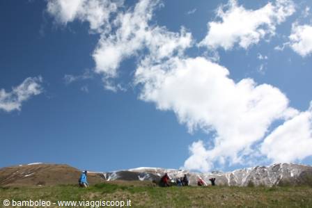 Hikers resting on grass beneath snowy peaks and white clouds