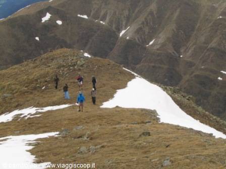 Hikers group walking on grassy ridge with snow patches and rocky peaks