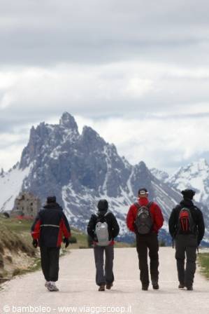 Hikers with backpacks walking on gravel road beneath snowy Dolomite peaks