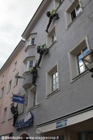 Helmeted climbers scaling the gray facade of a building, Sportler signs below