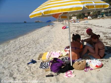 Girls in bikinis under a yellow striped umbrella reading on the sand