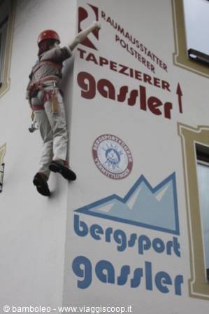 Climber in red helmet scales the painted facade of Bergsport Gassler shop