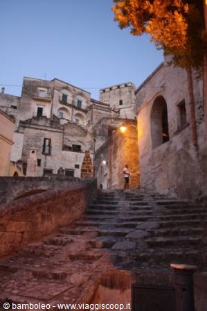 Stone staircase in the Sassi of Matera, a woman walks under a lantern
