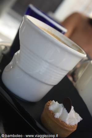 White coffee cup on black tray with a small cream tart