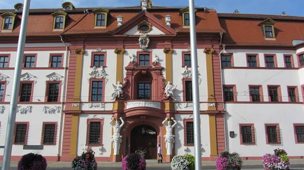 White and red Baroque facade with atlant statues and colorful flowers