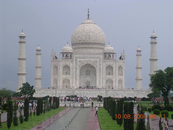 Visitors walk through the garden in front of the white marble Taj Mahal, grey sky