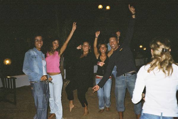 Group of friends dancing with raised arms at night, lit by lamps