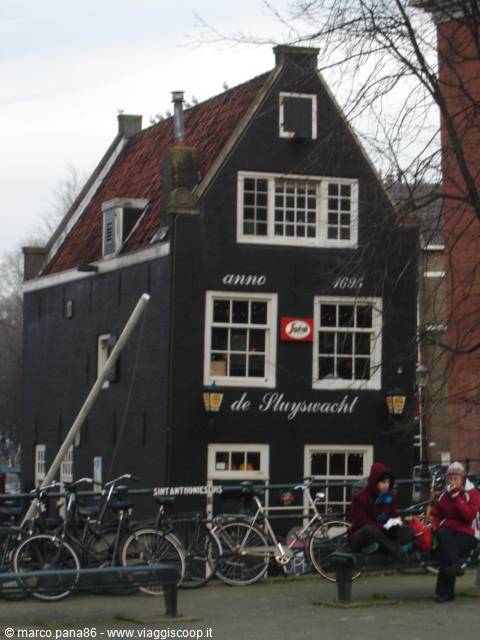 Cyclists passing the black wooden De Sluyswacht house, built 1695, Amsterdam