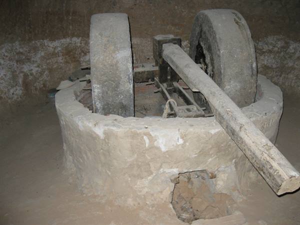 Ancient stone press with grinding wheels and wooden beam in dim light