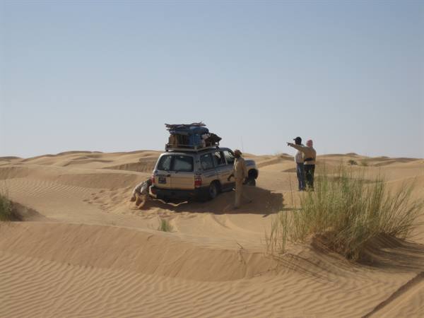 Loaded 4x4 stuck in sand, men push it among desert dunes
