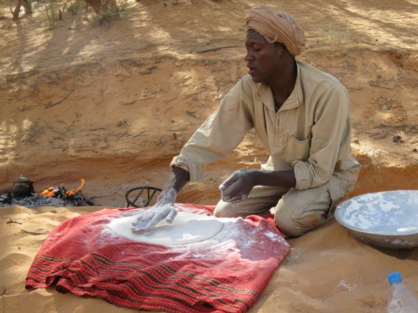 Man in turban flattens dough for bread on a red blanket in the sand