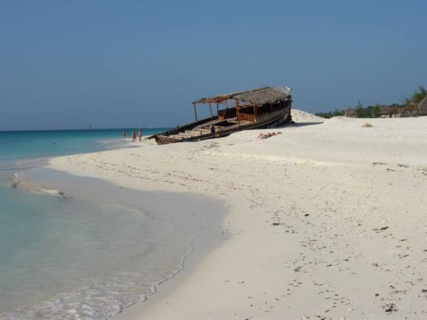 Wooden dhow stranded on white sand, tourists and turquoise water