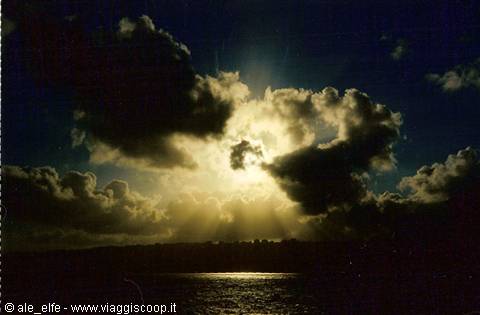 Sun breaking through dense dark clouds over the sea, golden reflections on water