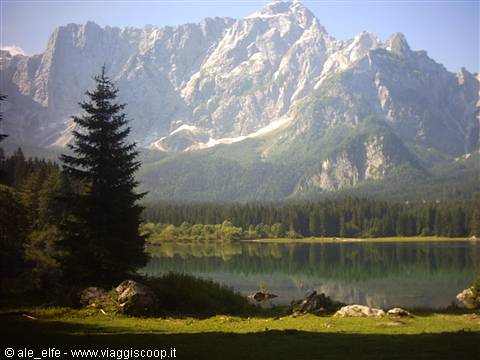 Lake Fusine with Mount Mangart reflected in the water among firs