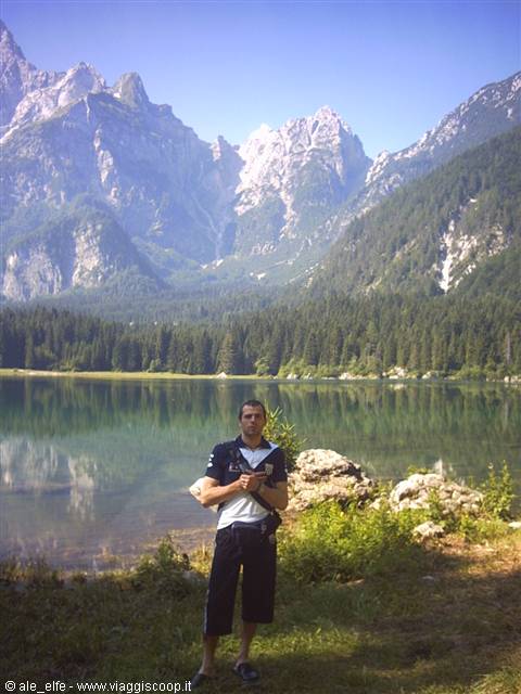 Tourist in white shirt posing on grassy shore of Fusine lake