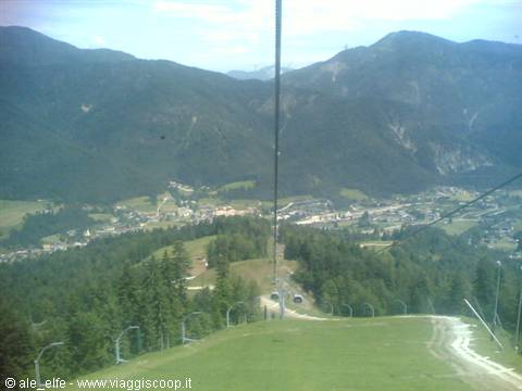 The cable car descends toward the village amid firs and green mountains