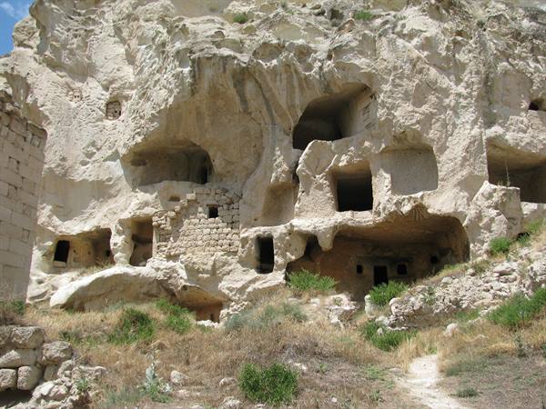 White rock-cut cave dwellings in Cappadocia, sunlight, dry grass below