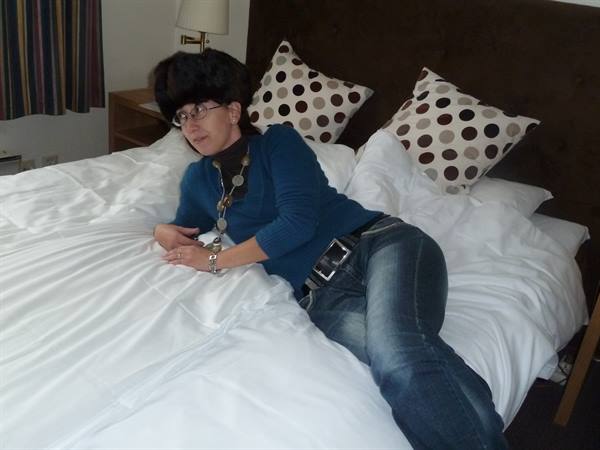 Woman in fur hat and jeans lying on a white hotel bed in Oslo